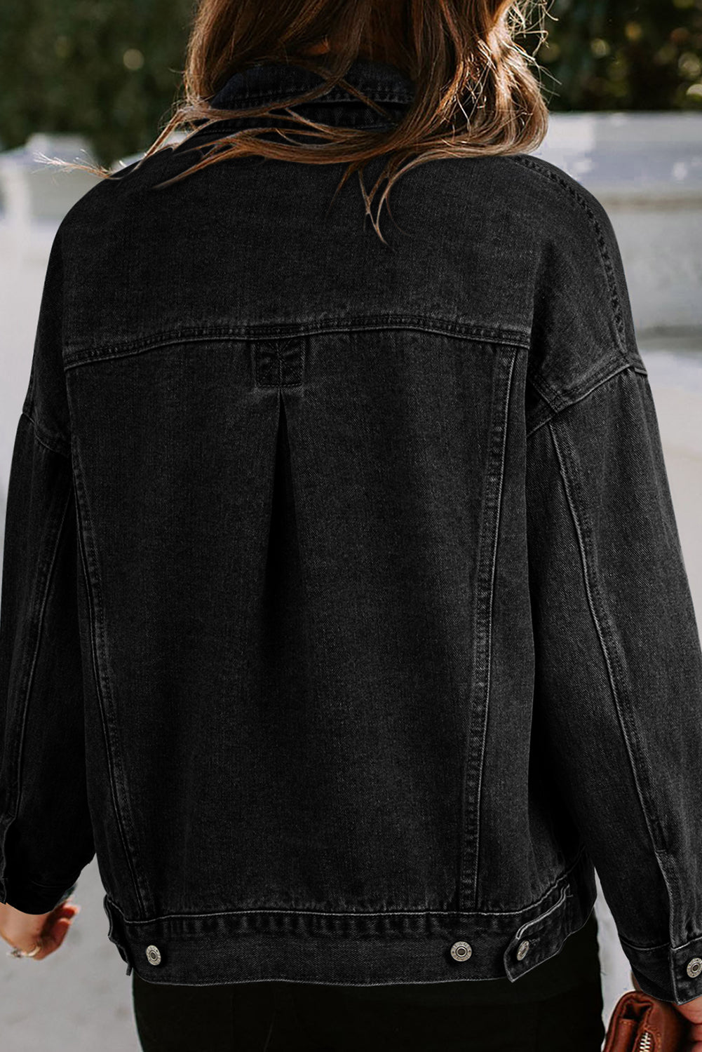 Dark-haired woman wearing the Black washed denim jacket. Oversized with button closure, turn down collar, and pockets. Back view