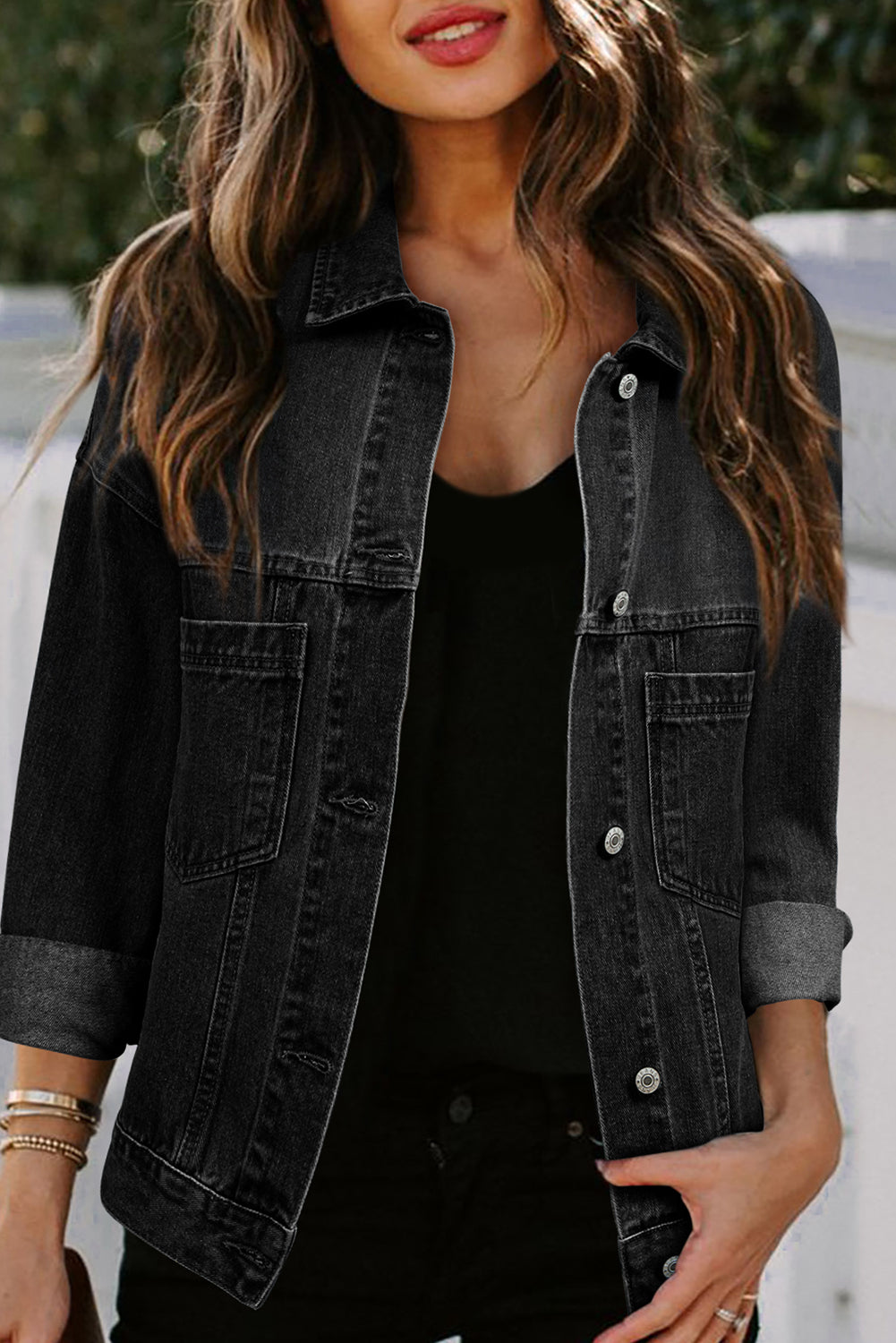 Dark-haired woman wearing the Black washed denim jacket. Oversized with button closure, turn down collar, and pockets. Front, open view