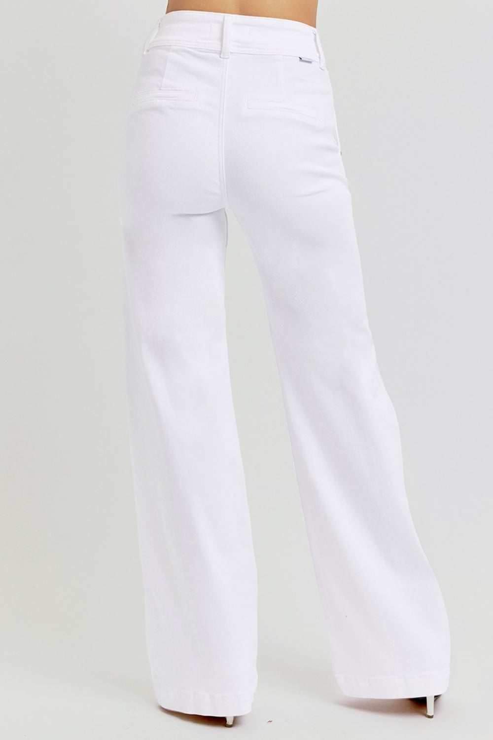 A person is showcasing the RISEN Tummy Control Double Button Wide Leg Jeans in a high-waisted, white design with a tailored fit and back pockets. The image highlights the classic wide-leg style reminiscent of traditional jeans, featuring a back view against a plain light gray background as the person stands confidently with both legs visible.