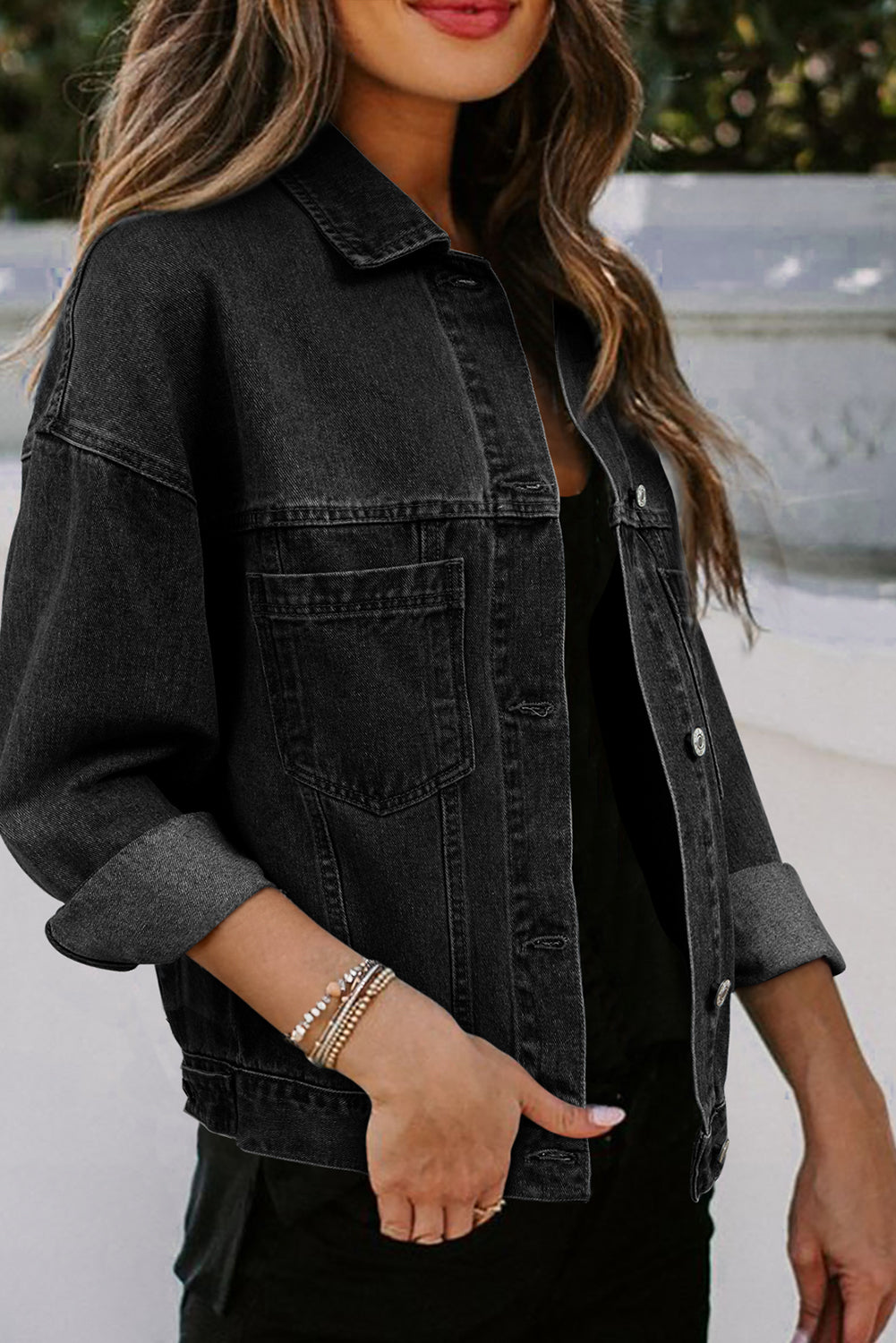 Dark-haired woman wearing the Black washed denim jacket. Oversized with button closure, turn down collar, and pockets. Front right, open view