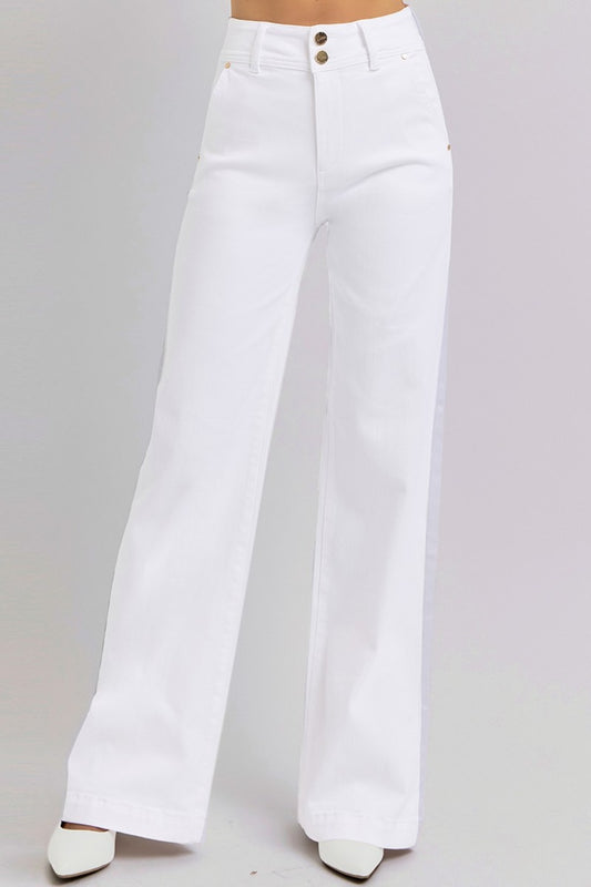 A person is standing against a light gray background wearing the RISEN Tummy Control Double Button Wide Leg Jeans, featuring a sleek, minimalist design in high-waisted, wide-leg style with pockets. Their feet are adorned in white pointed shoes that perfectly complement the structured high-rise waist and tailored look of the jeans.