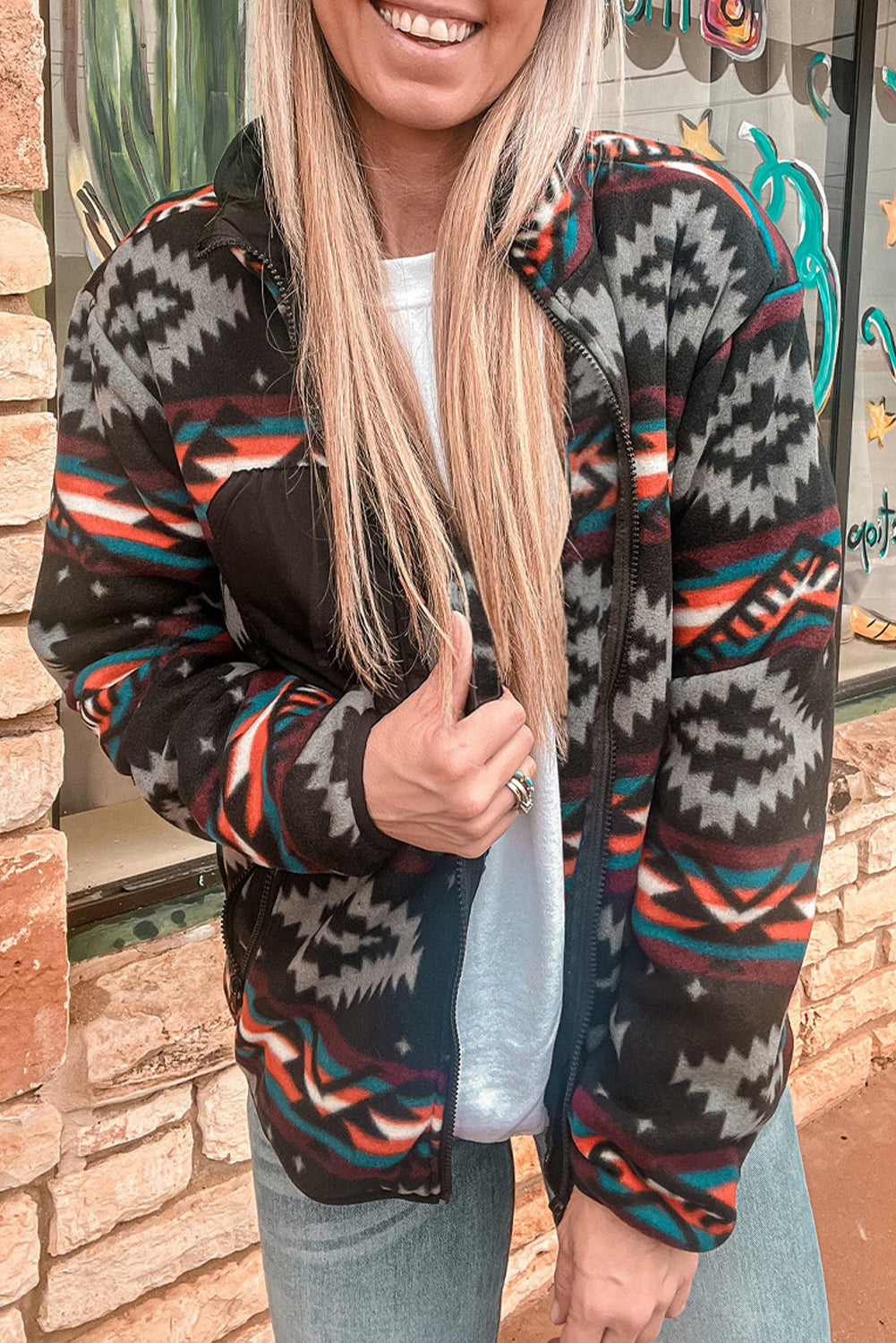 Woman wearing featured Aztec Printed Zip Up Jacket in Black and grey, paired with jeans and a t-shirt. Close up front view.